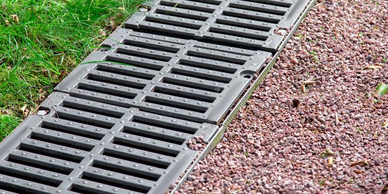 A picture of gravel next to a long drain to help with water flow to the right places.
