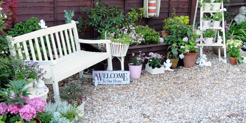 A picture of a nice gravel patio with a white bench and lighthouse decor.